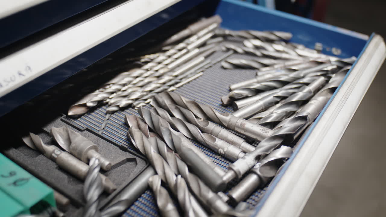 Close up shot of various steel drill bits inside an open blue metal drawer in an industrial workshop