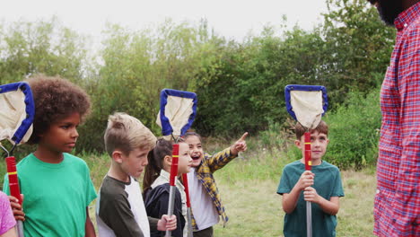 male team leader showing group of children on outdoor activity camp how to catch and study pond life