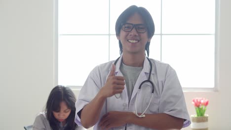 asian young male doctor showing thumb up while standing against window in the clinic