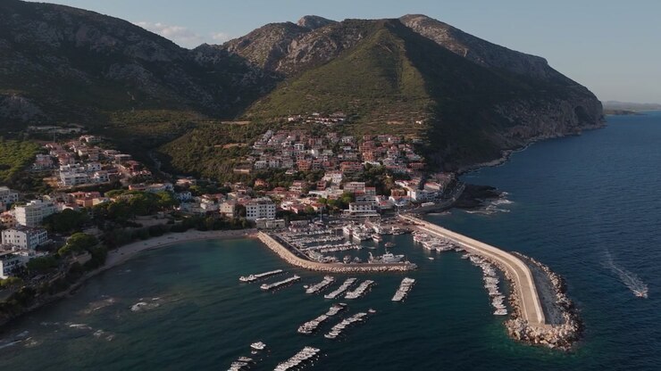 Sardenha, Porto de Cala Gonone; mostrando a cidade costeira, a marina, a paisagem montanhosa ao redor e a costa do Mediterrâneo, vista aérea cinematográfica