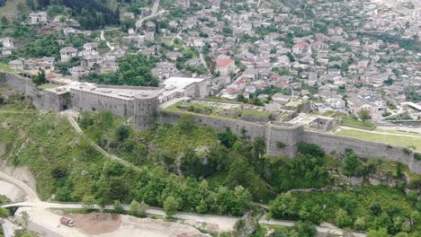 Drone-view-in-Albania-flying-in-Gjirokaster-town-over-a-medieval-castle-on-high-ground-fort-showing-the-brick-brown-roof-houses