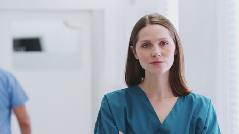 head and shoulders portrait of female doctor wearing scrubs in busy hospital corridor