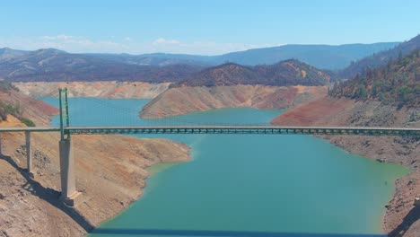 Beunruhigende-Luft-über-Dem-Von-Der-Dürre-Betroffenen-Kalifornischen-Oroville-see-Mit-Niedrigem-Wasserstand,-Zurückweichender-Küstenlinie-Und-Großer-Brückenüberquerung