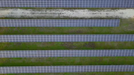Top-down-aerial-view-of-textured-solar-panel-farm-with-green-field---4k