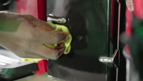 close-up of hand wiping black surface of red coffee machine with green cloth, focusing on cleaning and maintaining machine's surface for a spotless and shiny kitchen appliance