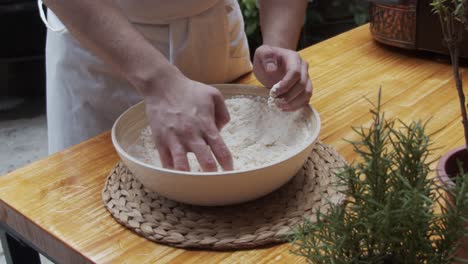 El-Chef-Moldea-La-Masa-De-Pizza-En-Un-Plato-Hondo,-Sobre-Una-Mesa-De-Madera