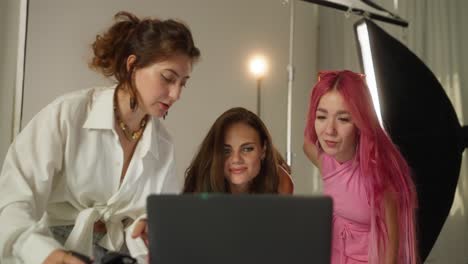 three women in a photo studio looking at a laptop