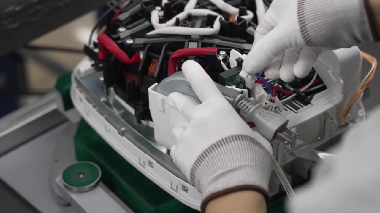 Assembly worker connecting motor component and electrical wires inside rice cooker body on production line