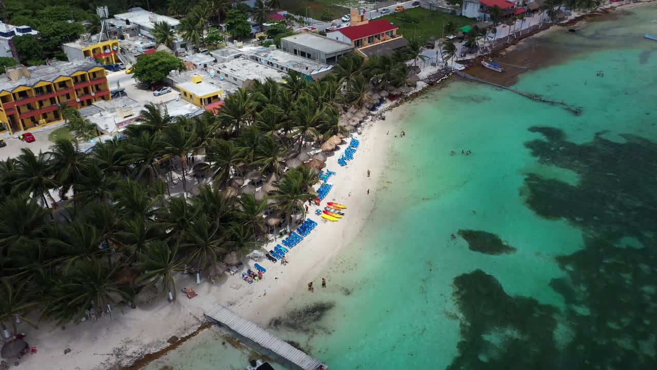 Impresionante vista aérea de Bacalar, México, con aguas cristalinas de laguna turquesa, playa bordeada de palmeras y cabañas con techo de paja. Escena de paraíso tropical con gente disfrutando de la costa caribeña