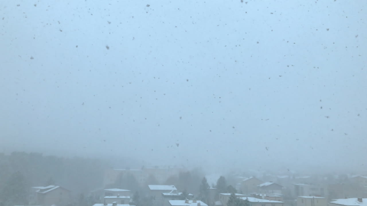 The view of the snow falling outside the window, white large snowflakes slowly fall to the ground, the first snow outside the window, winter weather conditions outside,