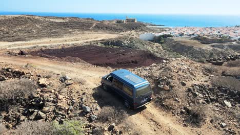 circling drone shot of cyan blue van on top of mountain in spain, ocean in background daytime