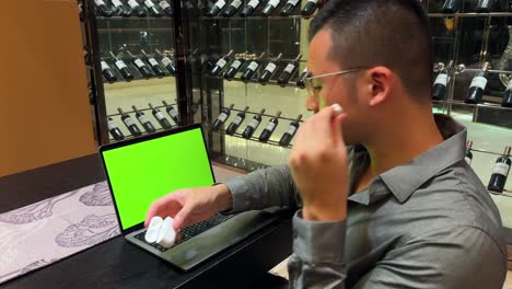 Wealthy-Asian-Millennial-Man-Nodding-Head-To-Music-In-Front-of-Laptop-Green-Screen-Inside-a-Luxurious-Home