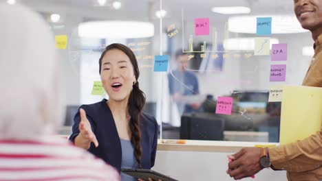 Group-of-diverse-business-people-taking-notes-on-glass-wall-and-talking-in-office,-slow-motion