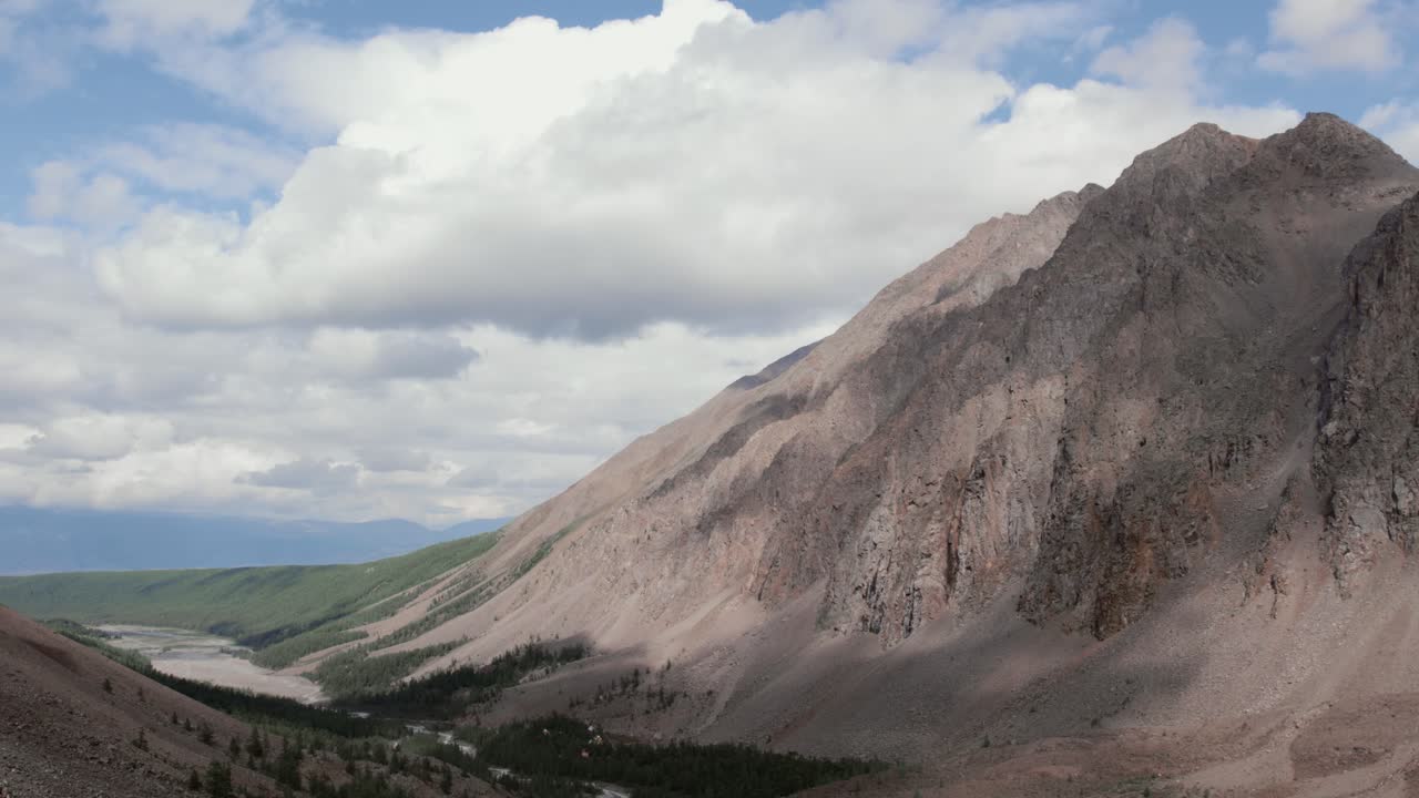Ampia vista panoramica di montagne aspre, una valle verde e un fiume serpeggiante sotto un cielo nuvoloso nella Valle di Aktru, Repubblica dell'Altai, Russia, ideale per temi di viaggio e natura.