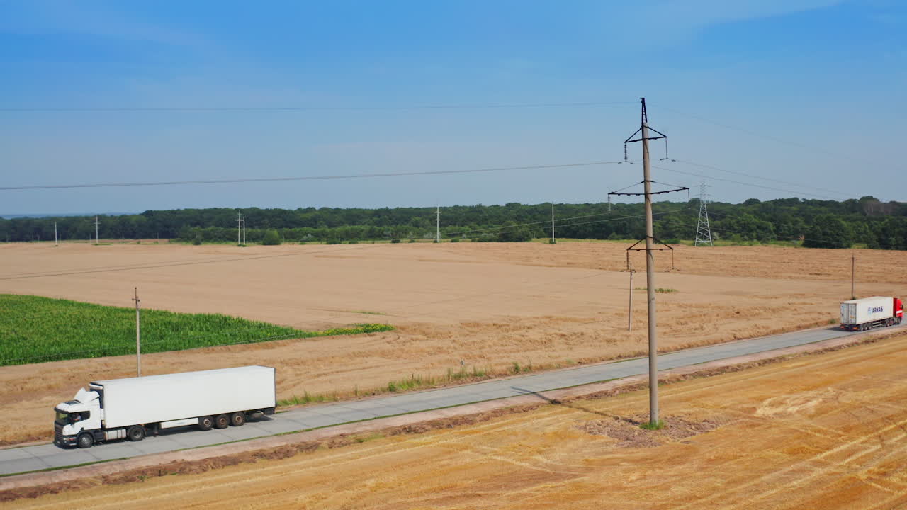 White truck going by the road crossing the farmlands. Agricultural machinery working in the field on harvest season. Top view.