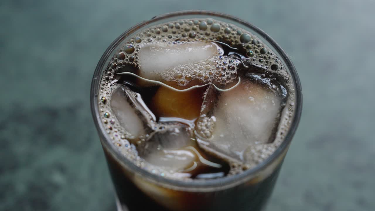 A close-up footage of stirring the ice cubes in an iced tea glass with a small spoon, with a blurred background