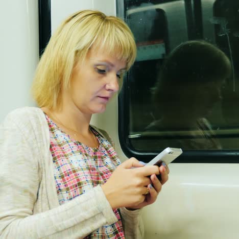 a woman rides in a subway car and uses a smartphone