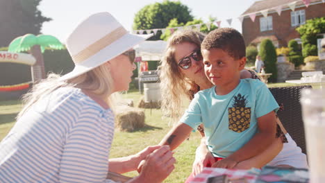 slow motion shot of young boy with mother at face painting stall at summer garden fete