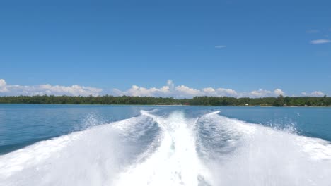 trails of a speed boat with tropical island in the background