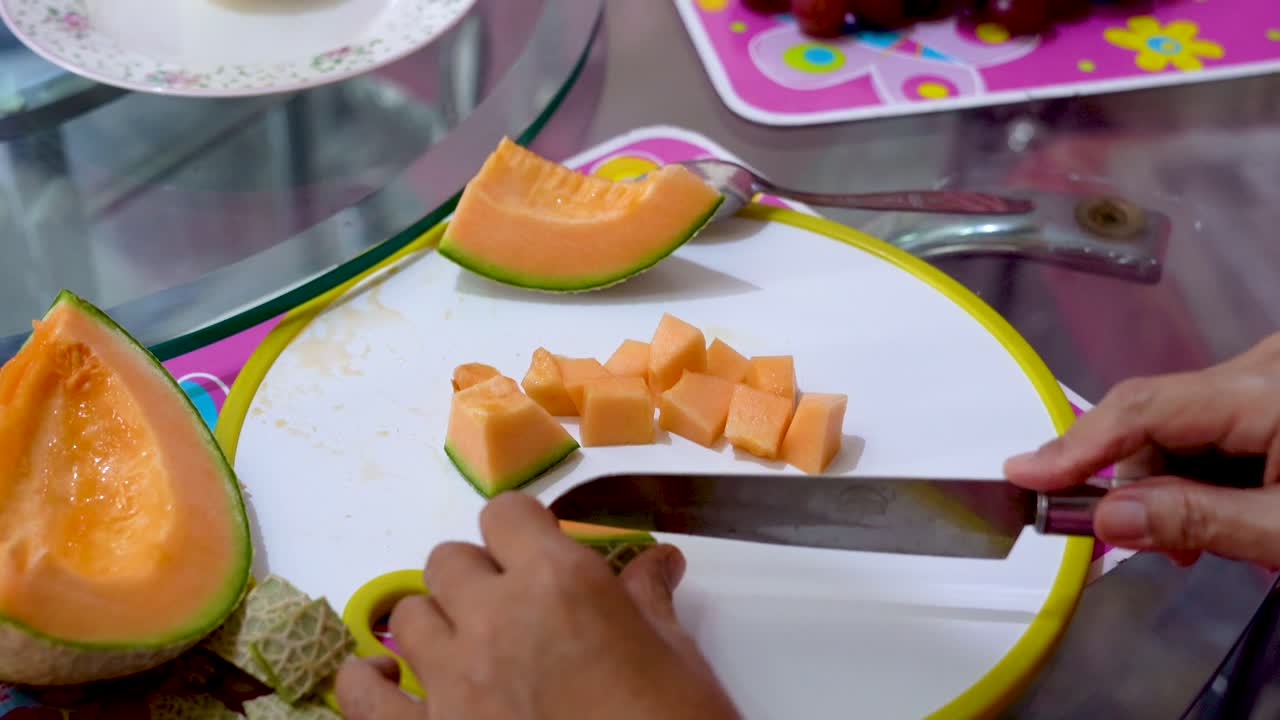 manos de mujer cortando melón dorado en trozos pequeños, vista de cerca