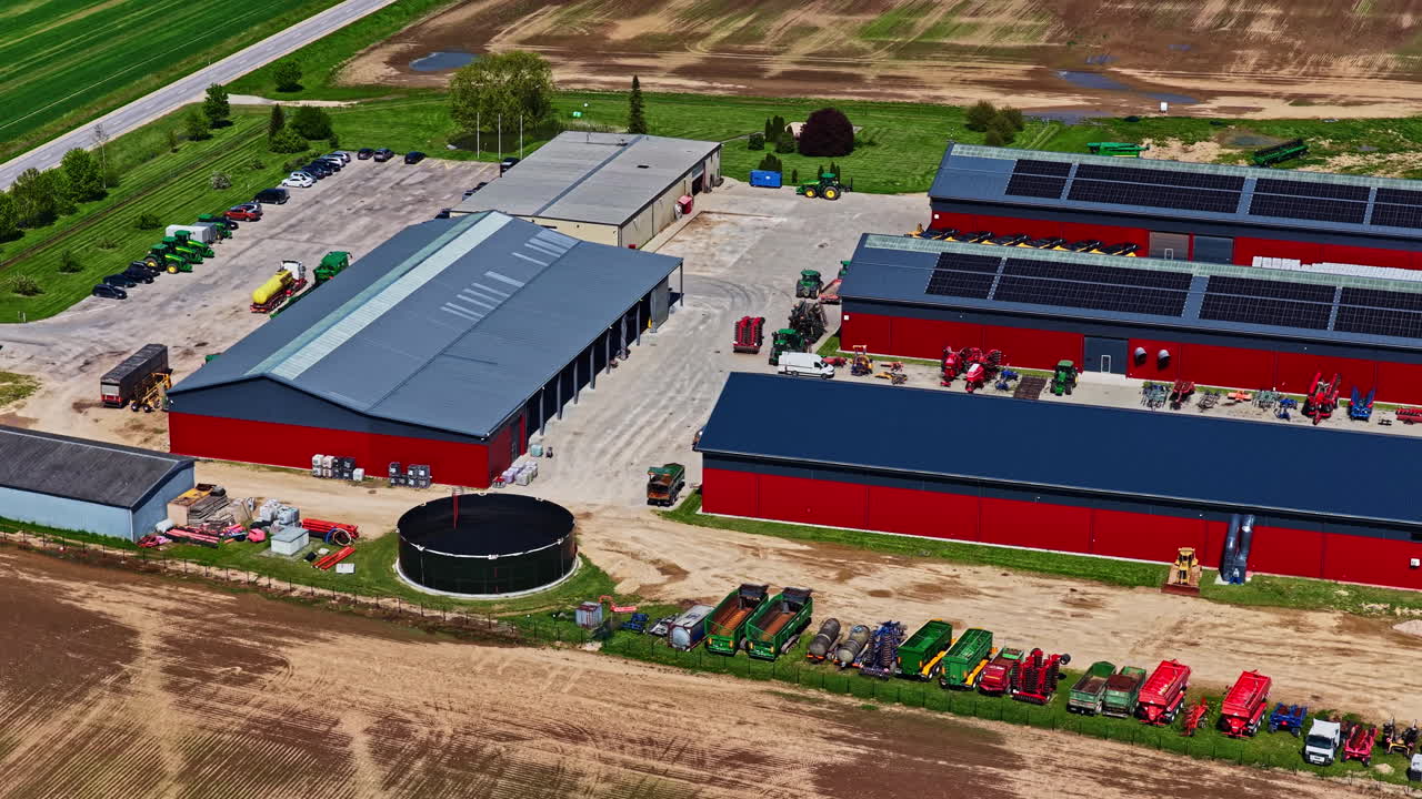Modern agricultural facility with red barns, solar panels, and farm machinery lined up