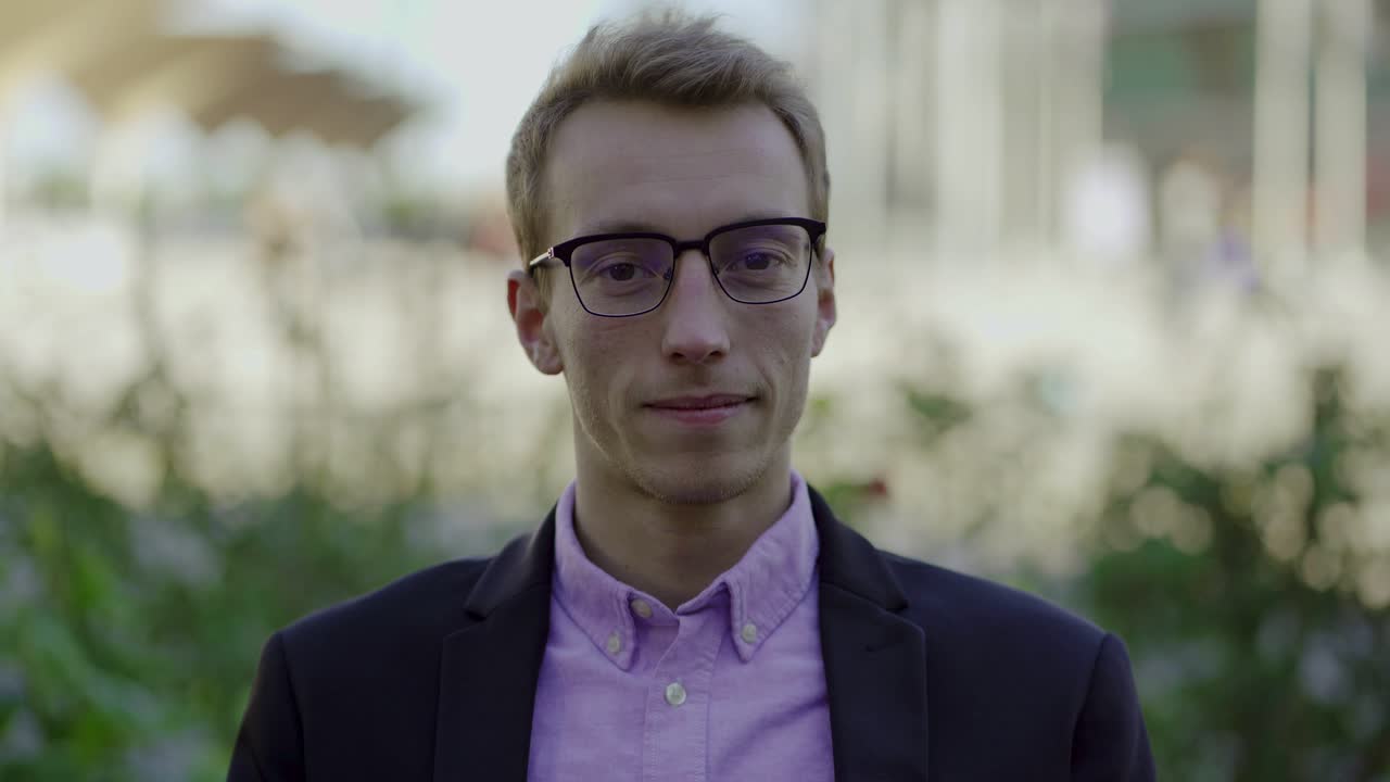 Giovane uomo sorridente e sicuro di sé, con gli occhiali, che guarda la fotocamera.