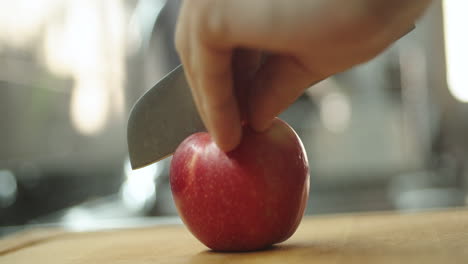 Young-guy-cutting-an-apple-on-wooden-table-in-kitchen-for-prepare-a-fruit-milkshake