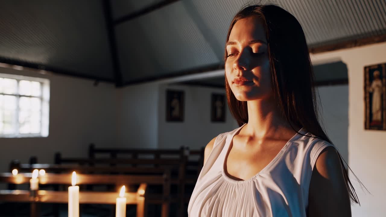 Young woman with closed eyes stands in a serene space illuminated by candlelight, embodying tranquility and introspection in a peaceful moment of reflection