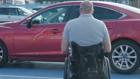young handicapped driver getting in red car from wheelchair