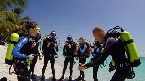 professional scuba diving instructor guiding diving team on pristine tropical beach, providing comprehensive safety briefing before ocean exploration with specialized equipment