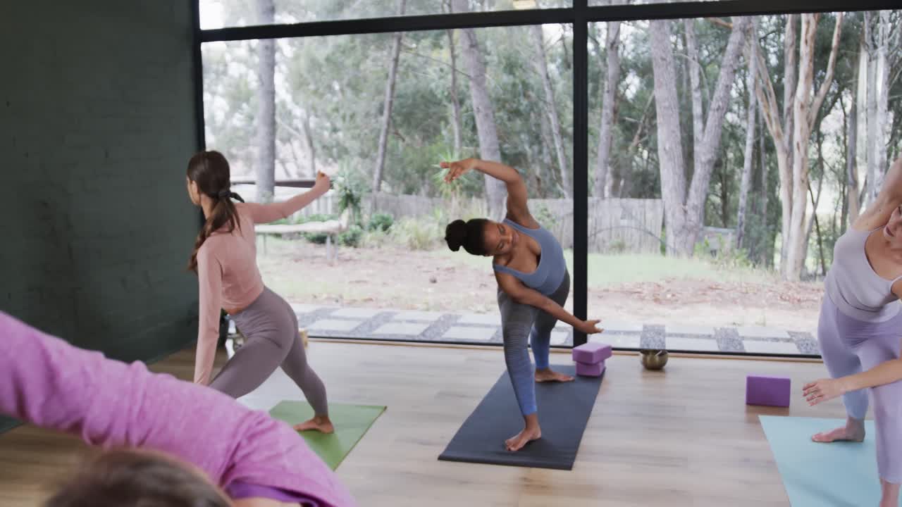 Donne diverse e concentrate che si allungano insieme sui tappetini in una lezione di yoga con l'istruttrice, al rallentatore