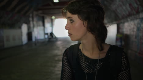 anxious young alternative style woman walking along dark underpass with graffiti covered walls on london city street uk in real time 2