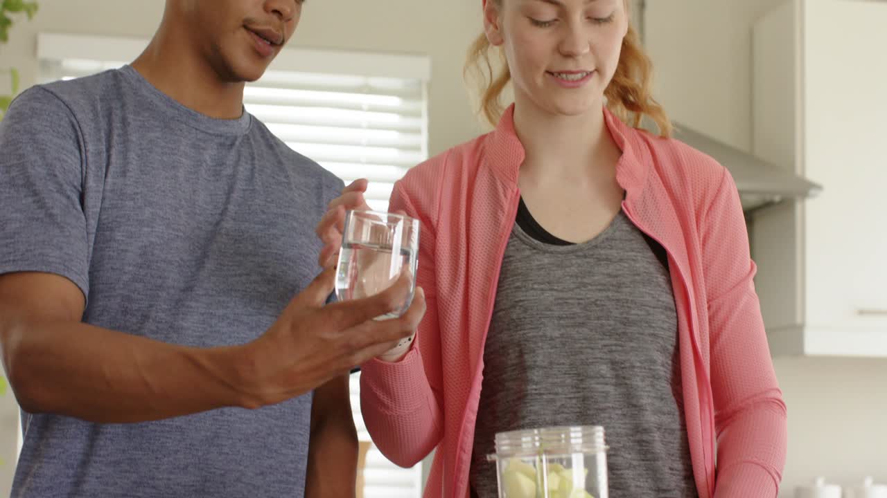 Diverse couple sliding glass then pouring water into blender cup on kitchen counter making smoothie