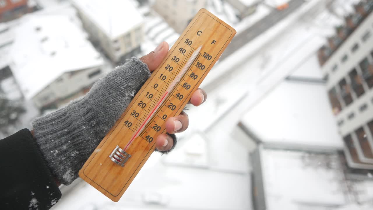 Hand holding a thermometer in snowy weather