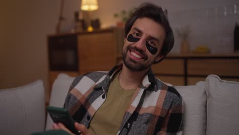 hombre relajándose con máscara para los ojos y teléfono inteligente en el sofá