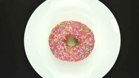 el donut rosado dulce gira en un plato. aislado en negro, vista de arriba