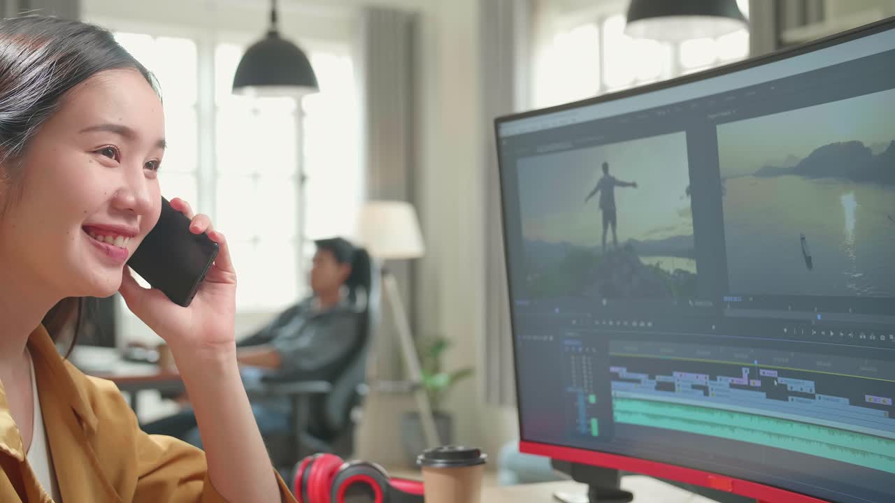 Asian Female Video Editor Works And Talking On Mobile Phone With Her Personal Computer In Office