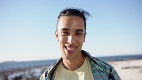 Portrait-of-happy-biracial-man-looking-at-camera-at-promenade-by-the-sea,-slow-motion