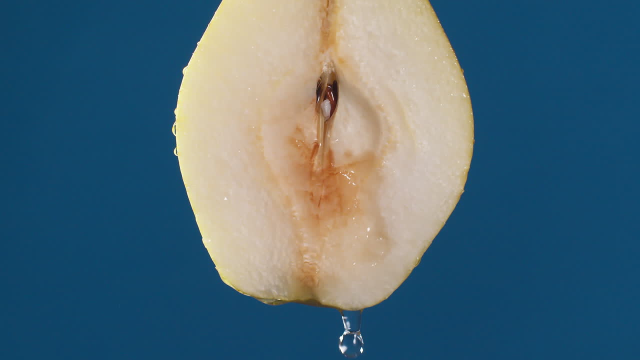 Yellow half pear on a blue dark background with drops of water rolling down the pear and flowing splashing with isolated background