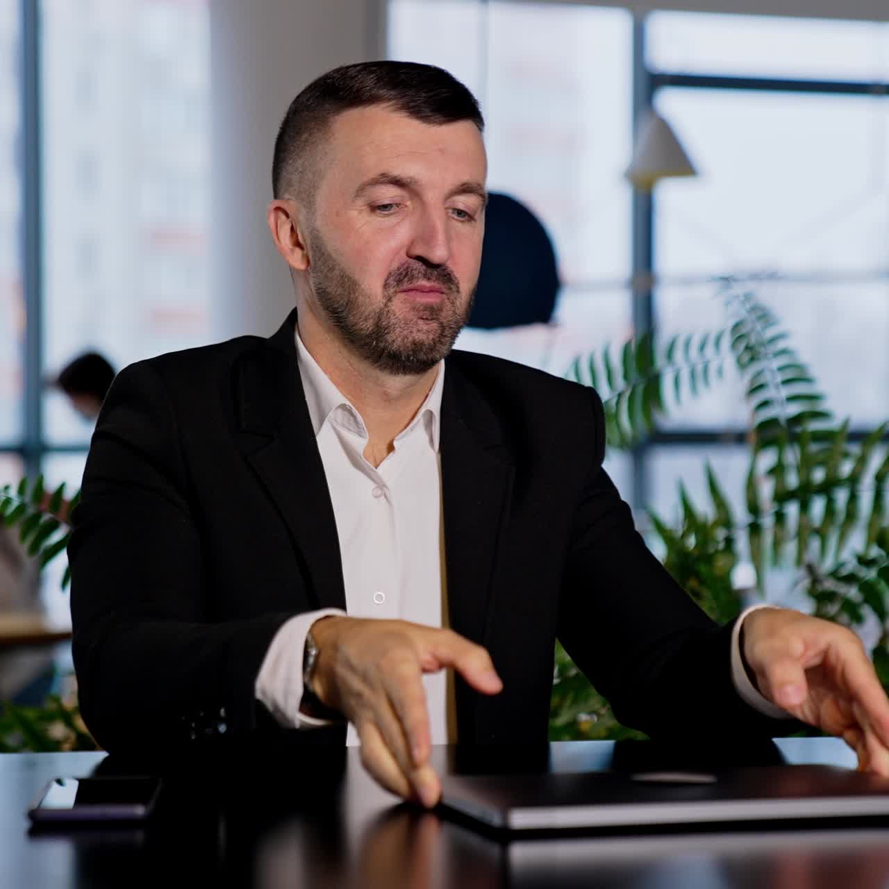 Smiling good-looking bearded man opens his laptop. Man changes in face when he can't open his computer. Blurred backdrop
