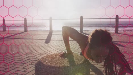 Pink-hexagonal-shapes-against-t-african-american-fit-woman-performing-push-ups-on-the-promenade