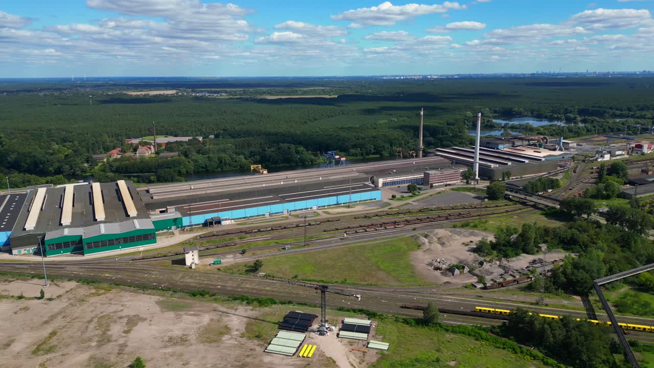 Hennigsdorf steel factory with chimneys, warehouses, railway, near river and forest in summer. Perfect aerial view flight panorama orbit drone