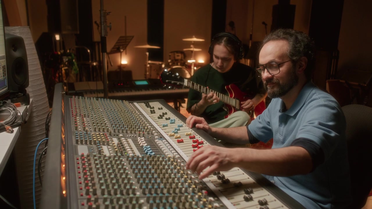 Sound Engineer Mixing Audio while Guitarist Playing Music in Recording Studio