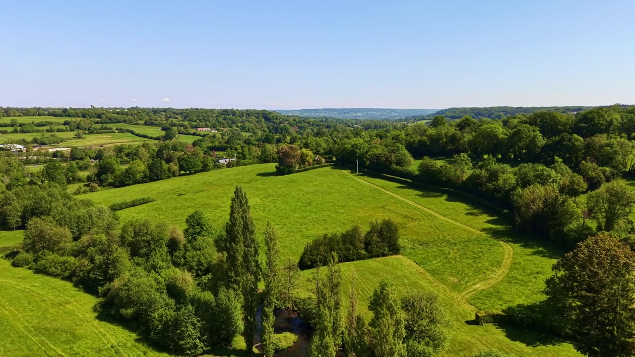 Wide aerial view of green rural fields and trees under clear blue sky in Normandy