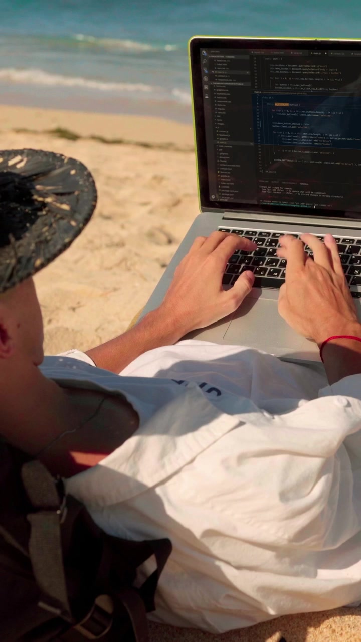 Caucasian developer coding on laptop while lying on sandy beach