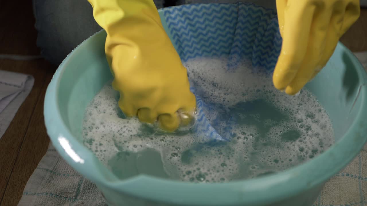 manos con guantes de goma con un paño y un recipiente con agua jabonosa tiro medio
