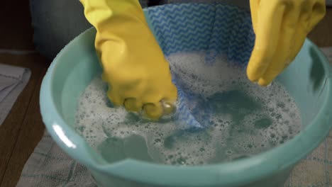 hands wearing rubber gloves with cloth and bowl of soapy water medium shot