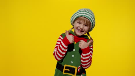 a little girl dressed as an elf smiles and gives a thumbs up