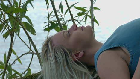 A-young-woman-is-lying-on-her-back-on-a-tree-branch-suspended-by-the-water