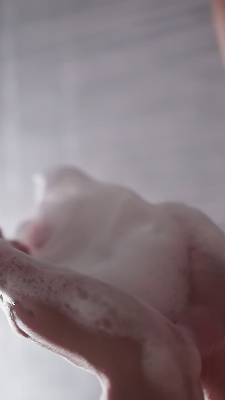 Woman plays with foam in shower cabin closeup. Playful lady blows heavy soap froth washing body in bathroom. Having fun during bathing procedures